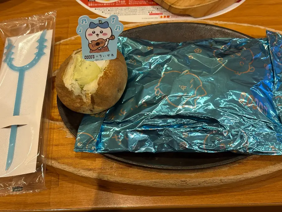 ココス×ちいかわ第2弾「ハチワレのクリームソース包み焼きハンバーグ」提供時の様子。ハチワレピック付きベイクドポテトと青いホイル包みのハンバーグが並ぶ。