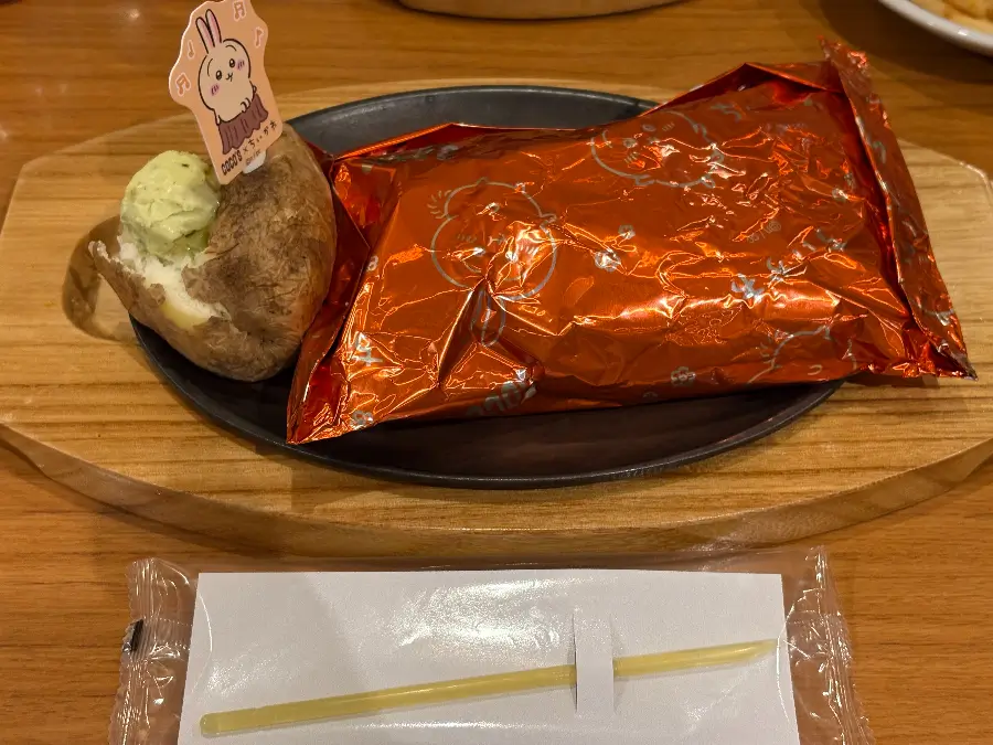 ココス×ちいかわ第3弾「うさぎのバターチキンカレー包み焼きハンバーグ」提供時の様子。うさぎピック付きベイクドポテトと黄色いホイル包みのハンバーグが並ぶ。